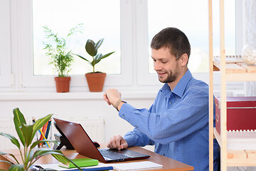 Image showing Business man in office looks at wristwatch with smile