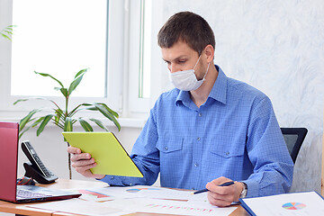 Image showing An office employee communicates in a tablet by video link, a medical mask is on his face