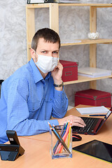 Image showing Worker working remotely in a computer in a medical mask looked into the frame