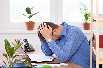 Image showing Office employee clutching his head in his hands while reading a document.