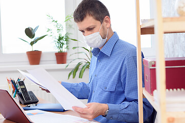 Image showing Office worker in protective medical mask works with documents in the office