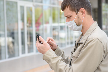 Image showing A man in a medical mask dials a number in a mobile phone, close-up