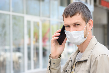 Image showing Portrait of a man in a medical mask with a mobile phone on the background of the store, looking in frame