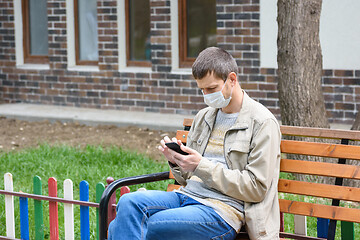 Image showing A man on the street crouching on a bench looks at the phone screen