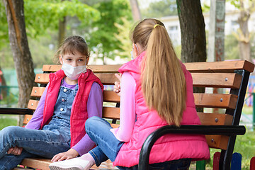 Image showing Girlfriends with face masks talk while sitting on a bench in the playground
