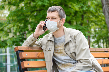 Image showing A man in a medical mask is talking on the phone in a park