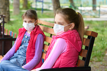 Image showing Two girls in medical masks sit on a bench in a park