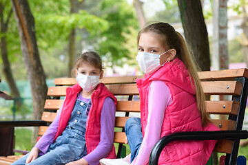 Image showing Girls in medical protective masks sit on a bench in the playground