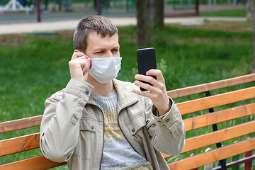 Image showing A man in a medical mask sits on a bench and adjusts the mask