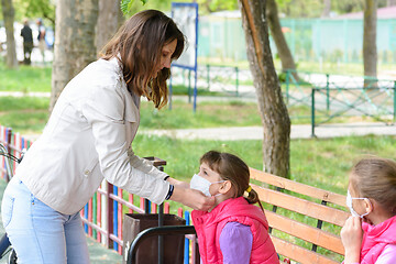 Image showing Mom puts a mask on her daughters face in the playground