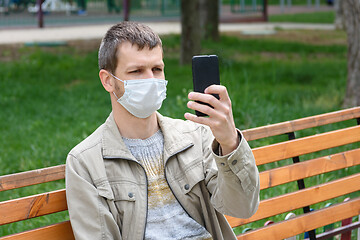 Image showing A man in a medical mask sits on a bench and photographs himself