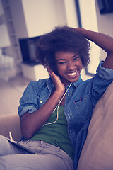 Image showing African american woman at home in chair with tablet and head pho