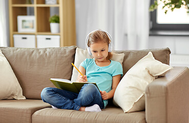 Image showing girl in headphones with diary on sofa at home