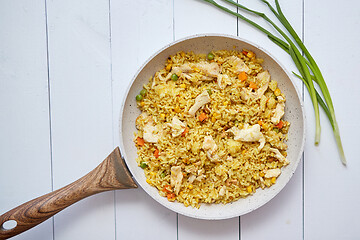 Image showing Delicious fried rice with chicken and vegetables served in pan. Placed on white wooden table