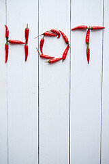 Image showing A word HOT formed with small red chilli peppers. Placed on white wooden table