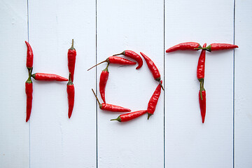 Image showing A word HOT formed with small red chilli peppers. Placed on white wooden table