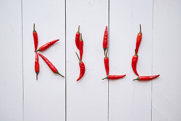 Image showing A word KILL formed with small red chilli peppers. Placed on white wooden table