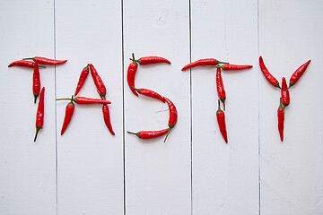 Image showing A word TASTY formed with small red chilli peppers. Placed on white wooden table