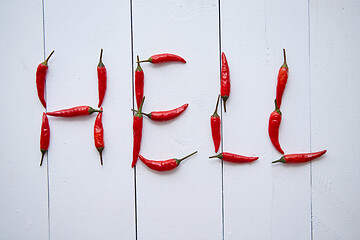 Image showing A word HELL formed with small red chilli peppers. Placed on white wooden table