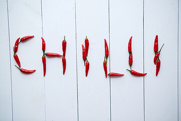 Image showing A word CHILLI formed with small red chilli peppers. Placed on white wooden table