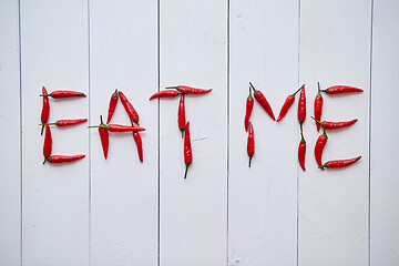 Image showing A word EAT ME formed with small red chilli peppers. Placed on white wooden table