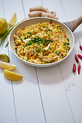 Image showing Delicious fried rice with chicken and vegetables served in pan. Placed on white wooden table