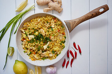 Image showing Delicious fried rice with chicken and vegetables served in pan. Placed on white wooden table