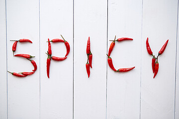 Image showing A word SPICY formed with small red chilli peppers. Placed on white wooden table