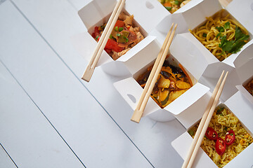Image showing Various oriental dishes packed in paper box. Food is delivered on the table. Asian take away concept