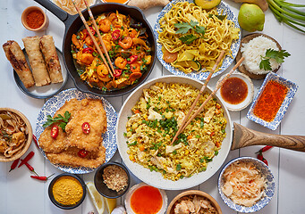 Image showing Asian food served. Plates, pans and bowls full of noodles chicken stir fry and vegetables