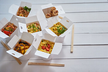 Image showing Various oriental dishes packed in paper box. Food is delivered on the table. Asian take away concept