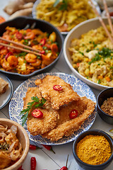 Image showing Asian food served. Plates, pans and bowls full of noodles chicken stir fry and vegetables