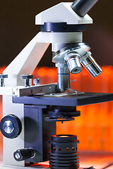 Image showing Close up of microscope lenses focused on a specimen in warm orange light light.