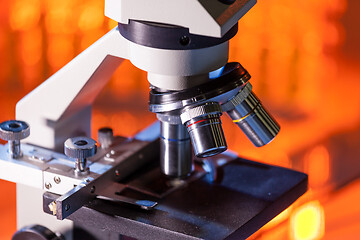 Image showing Close up of microscope lenses focused on a specimen in warm orange light light.