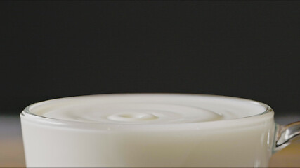 Image showing Milk drops drip into a cup with organic milk making splash around a dark background. Slow motion, Full HD video, 240fps, 1080p.