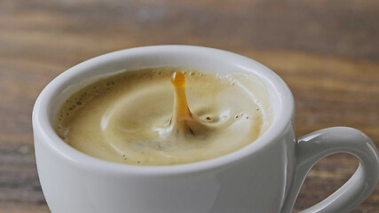 Image showing Close-up in a cup of fragrant espresso with foam fall coffee splash on a brown wooden table. Slow motion, Full HD video, 240fps, 1080p.