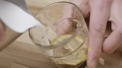 Image showing Barista hands pouring milk into a glass of coffee on a wooden brown table. Slow motion, Full HD video, 240fps, 1080p.