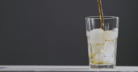 Image showing In a glass with ice pour coffee with splashes and bulbaki around dark background.