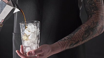 Image showing A man with a tattoo pours coffee in a glass with ice around a dark background. 4K UHD video, 2160p.