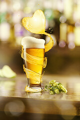 Image showing Flying heart splash of light beer above glass of fresh beverage.