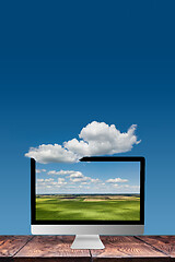 Image showing Monitor with landscape on a wooden table and blue sky background.