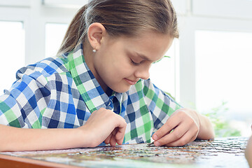 Image showing Passionate girl collects puzzles at home at the table