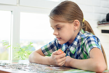 Image showing Girl collects a puzzle while sitting at home at the table and eats carrots