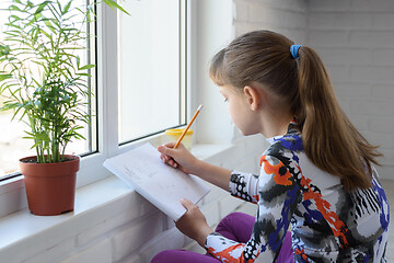 Image showing A teenager draws with a pencil in an album sitting on the floor in front of the window