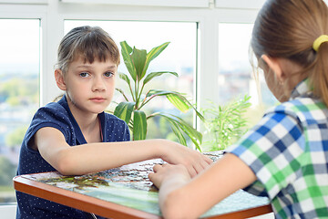 Image showing Sad girl collects puzzles in the company of girlfriends and looked into the frame