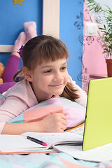 Image showing The girl is remotely studying at home, lying in bed and watching a video lesson