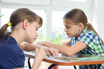 Image showing Two girls enthusiastically collect puzzles at the table at home