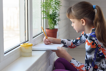 Image showing The child draws with a pencil on the windowsill at home