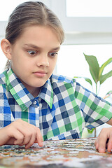 Image showing Girl in surprise looks at the puzzle on the table