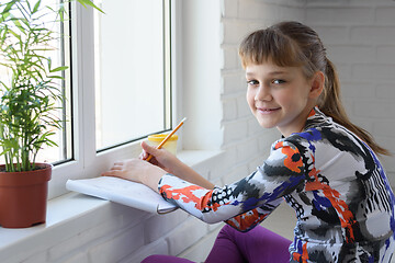 Image showing The girl draws sitting on the floor by the window and looked into the frame with a smile